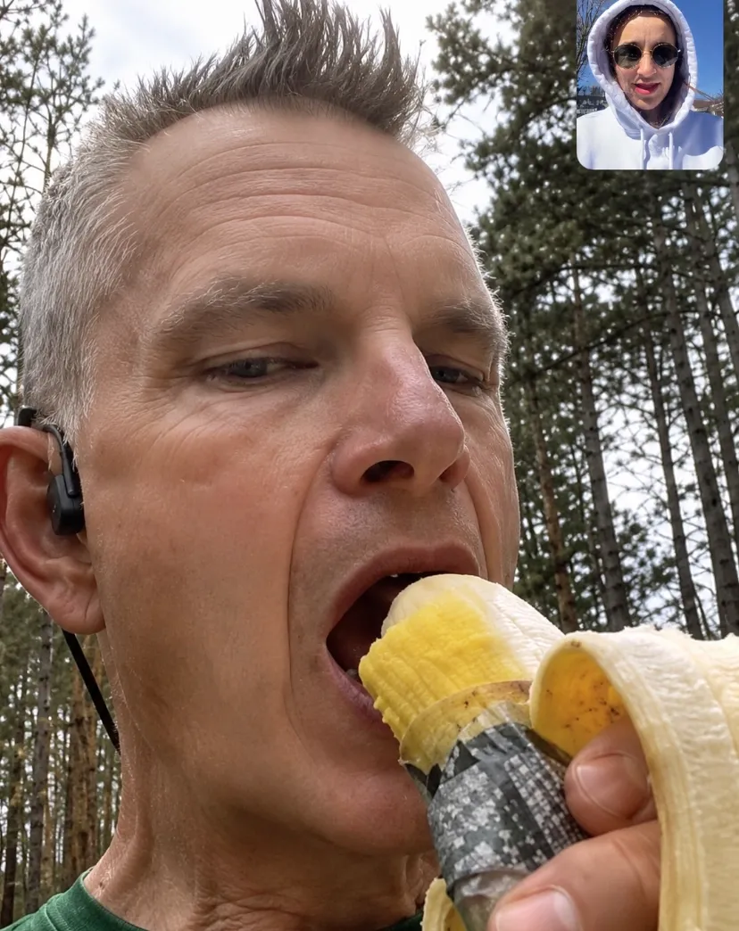 Kyle eating a banana mid-race while on FaceTime with his daughter, pickle juice in the other hand