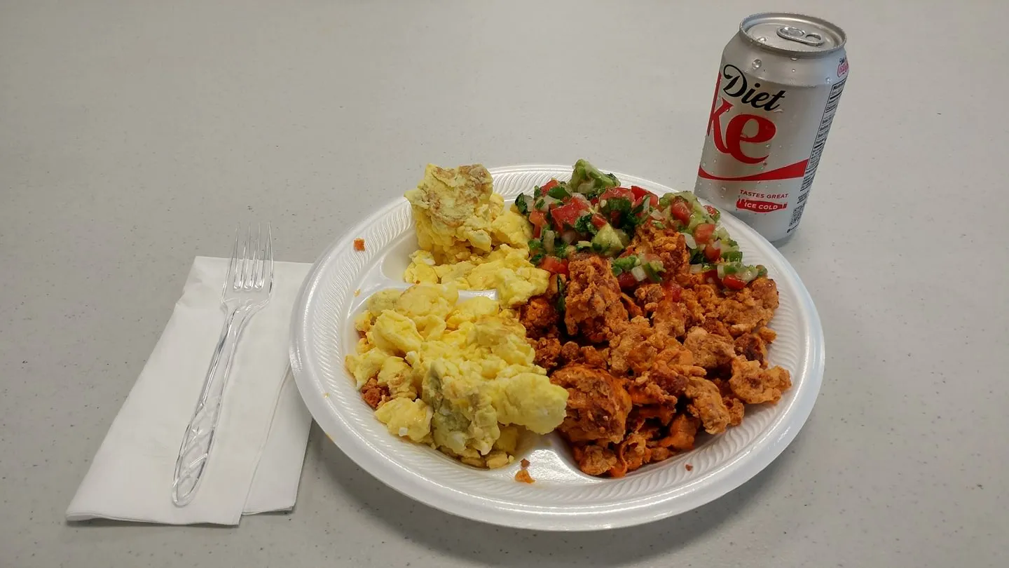 Paper plate of scrambled eggs, seasoned meat, and pico de gallo beside a Diet Coke