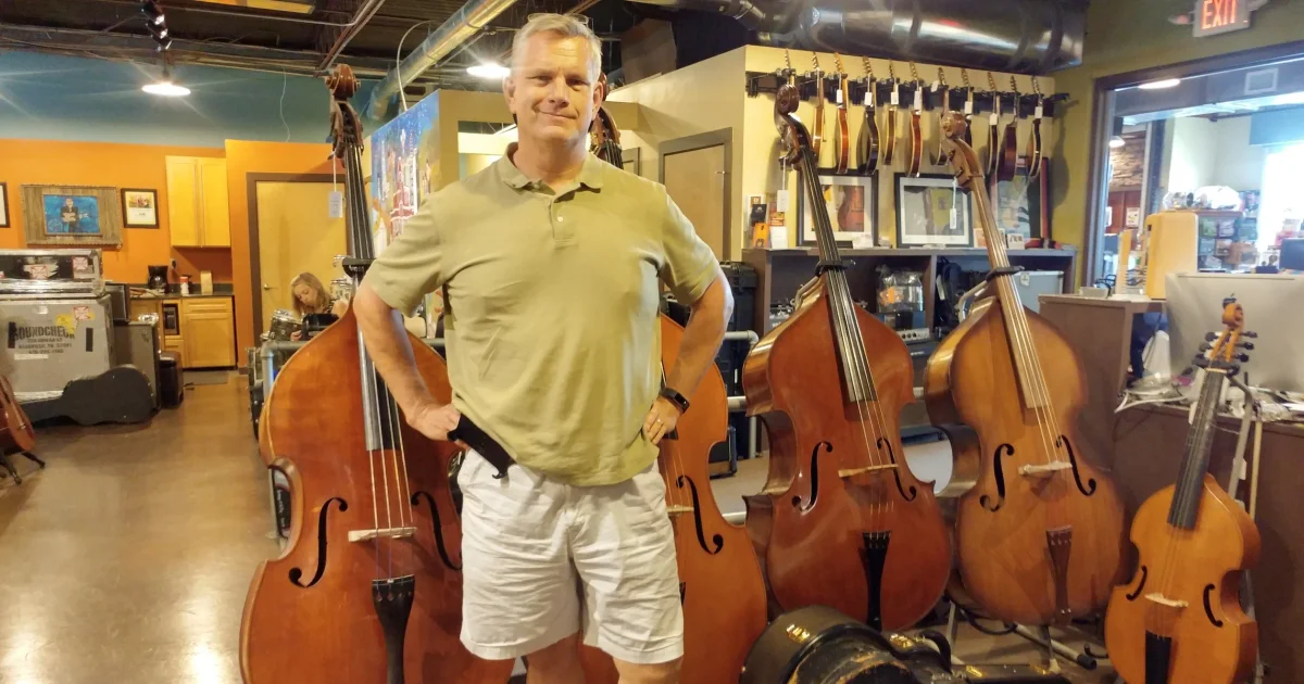 Kyle at Carter's Vintage Guitars in Nashville, standing among a row of double basses